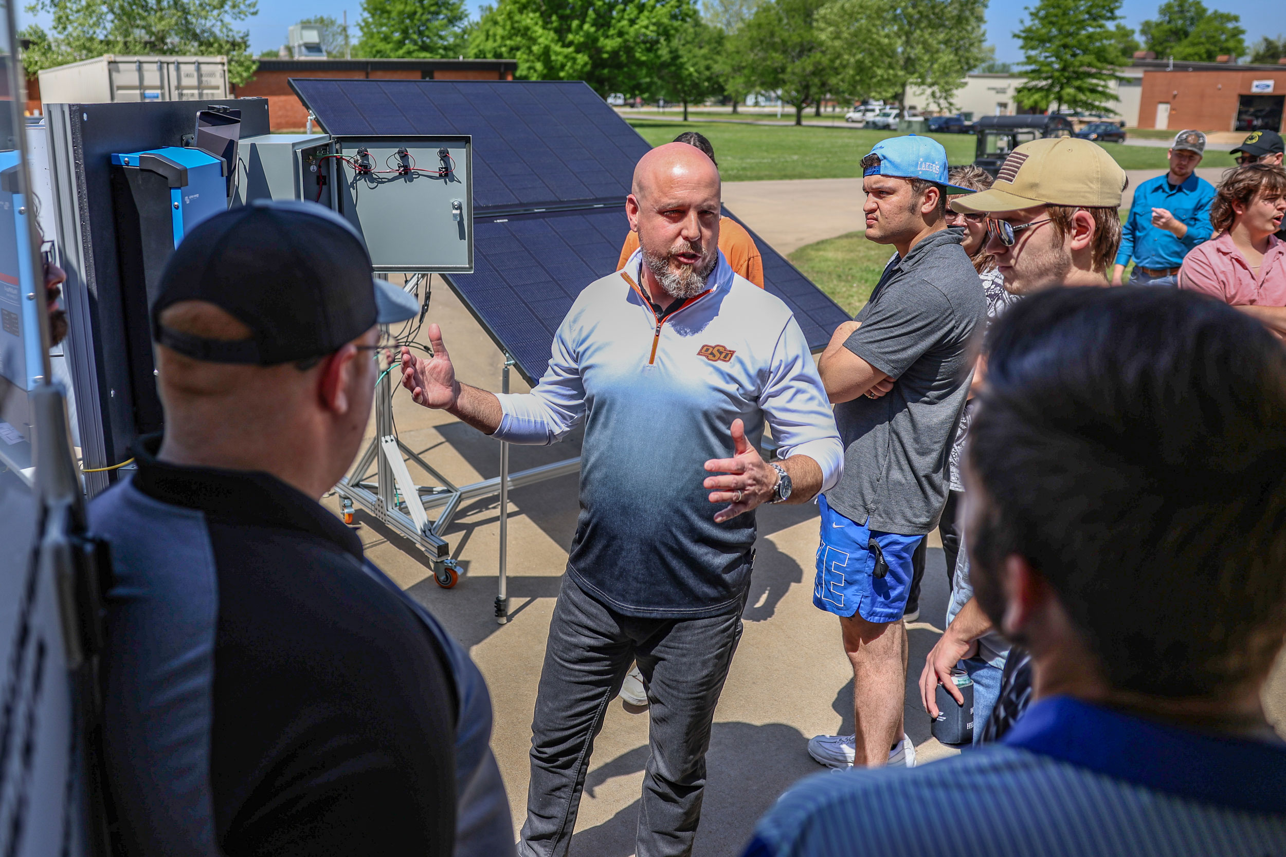 A group of OSUIT students attentively listening to an instructor explain solar panel technology during an outdoor hands-on class, with solar panels and equipment in the background.