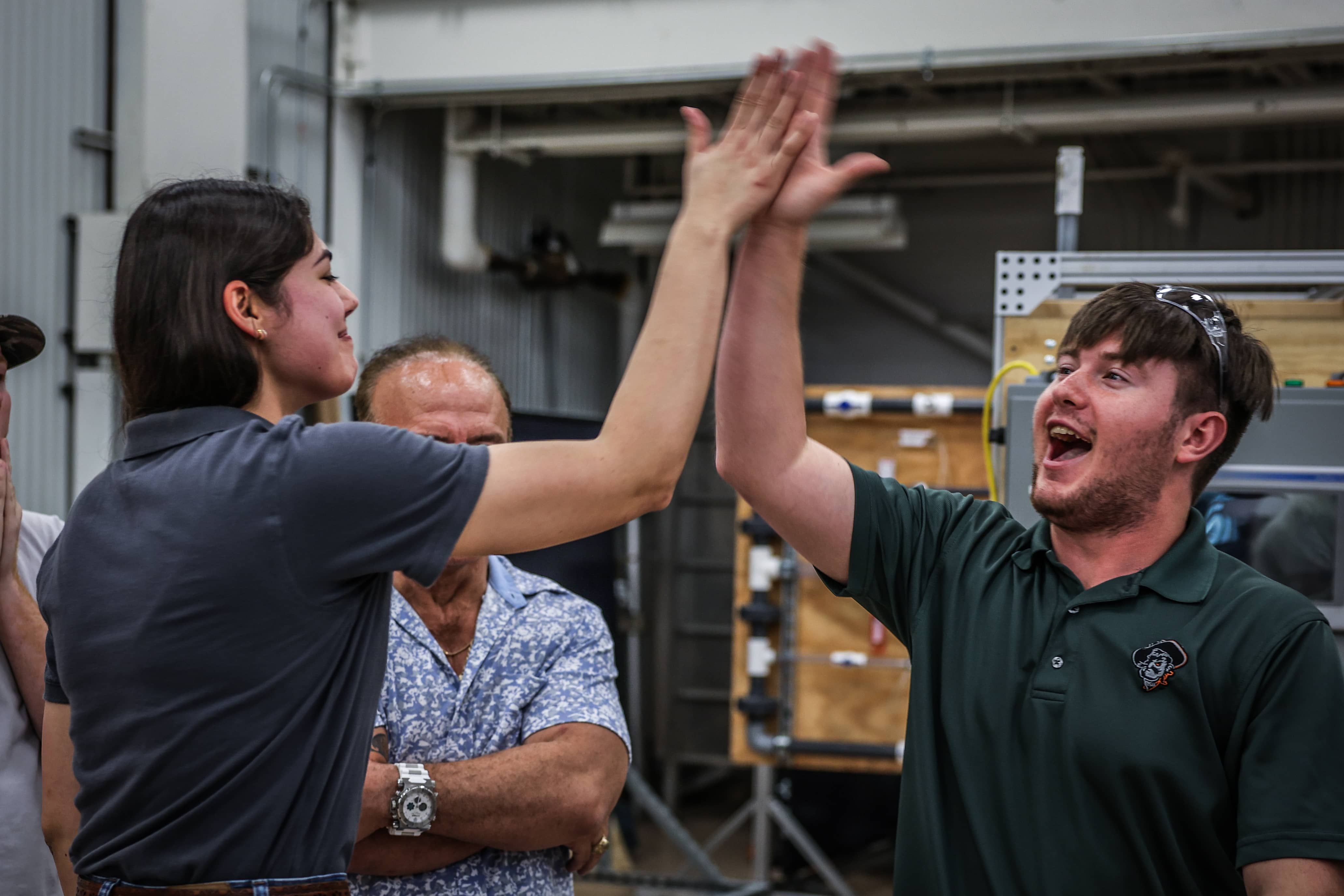 Two OSUIT students high-fiving each other in a lab, with an instructor and another student looking on, smiling.
