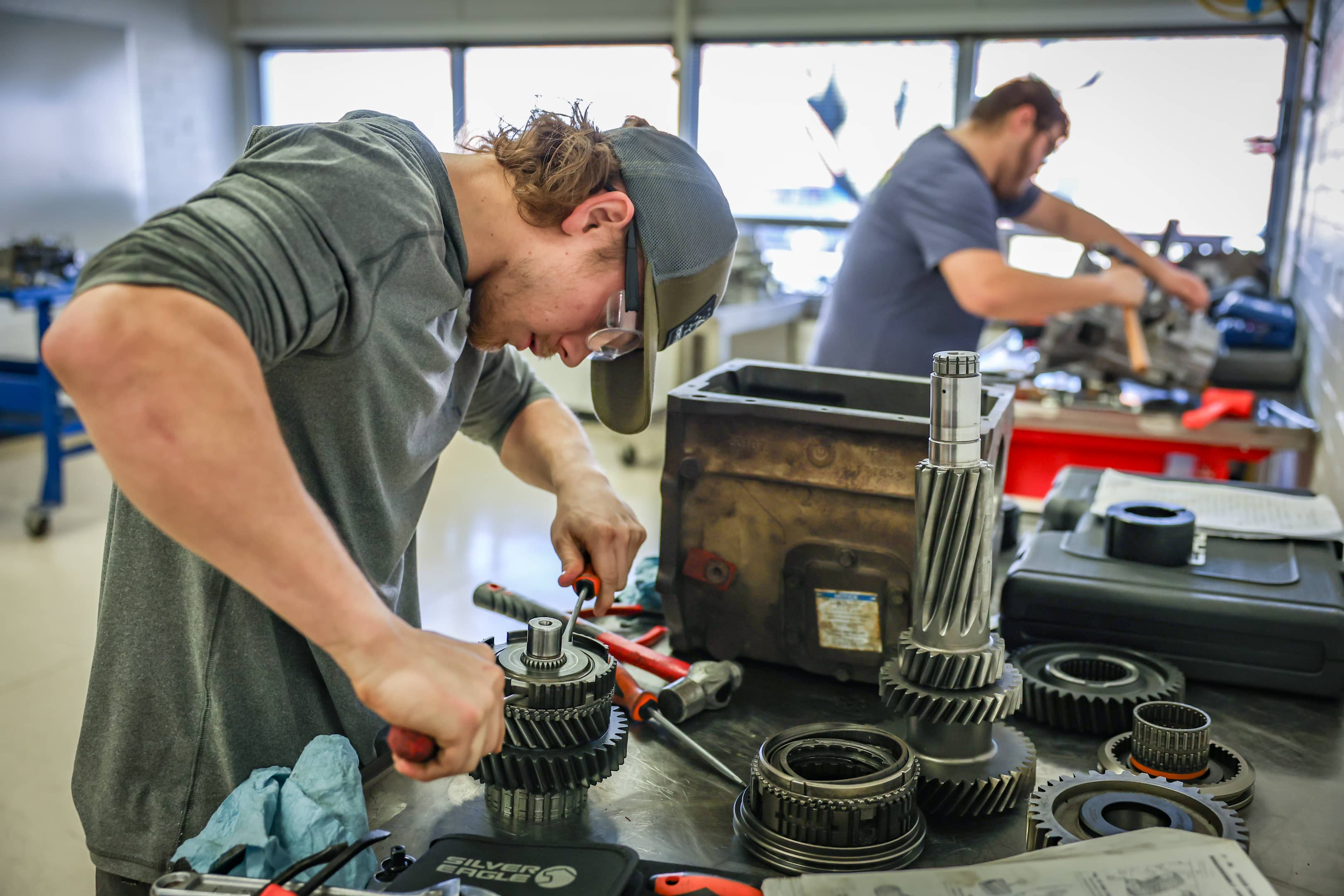Two OSUIT students working on gear assemblies in a mechanical engineering lab, focusing intently on their tasks.